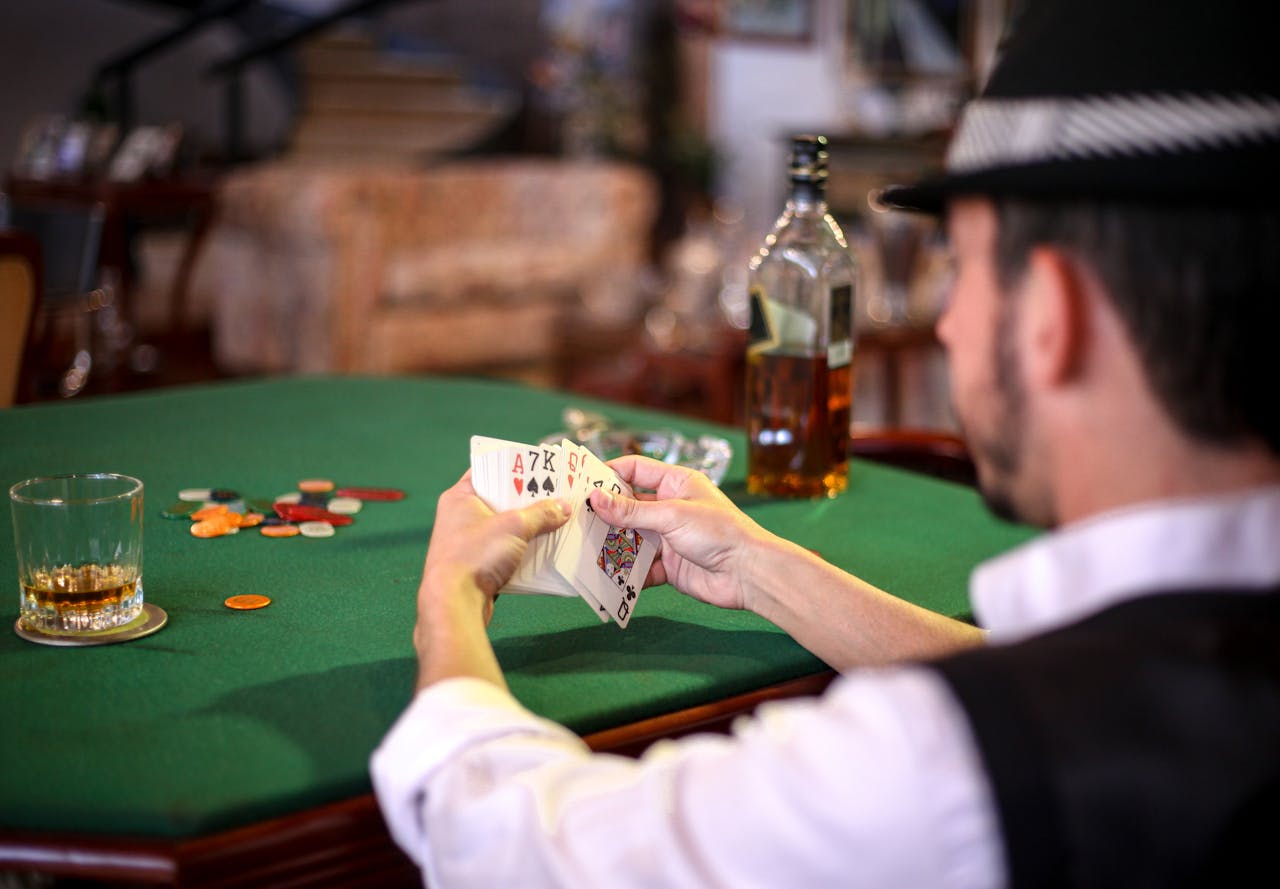 our-services-1 A man holding a poker hand at a casino table with chips and whiskey, conveying a gambling atmosphere.