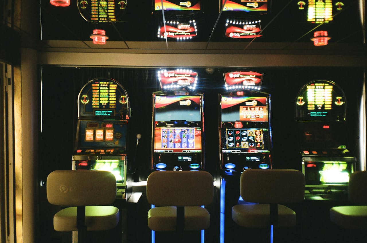 our-experience Slot machines in a dimly lit casino with reflective ceiling and empty chairs.